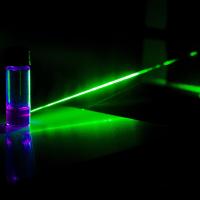 Green laser striking vial of liquid, with beam changing colour as it passes through.